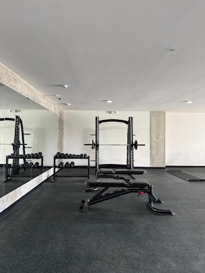 Un gimnasio con equipo de levantamiento de pesas, una banca y un espejo en la pared.