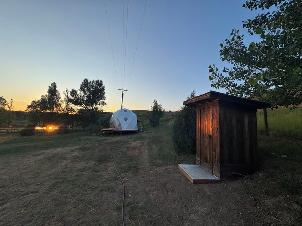 A rural setting with a wooden structure, a white dome tent, and a clear sky. - Unique Geodesic Dome overlooking the iconic Missouri River (Great Falls)