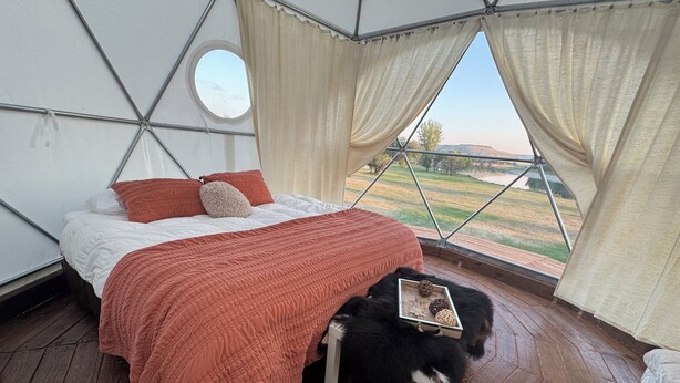 A tent-style room with a bed, a window with curtains, and a view of the outdoors.