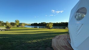 A tent with a circular window, a wooden deck, and a view of a river and trees.