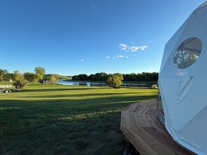 A tent with a circular window, a wooden deck, and a view of a river and trees. - Unique Geodesic Dome overlooking the iconic Missouri River (Great Falls)