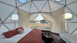 A yurt with a bed, a small table, and a view of a lake.