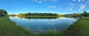 A calm lake with a grassy shoreline and trees in the background. - Unique Geodesic Dome overlooking the iconic Missouri River (Great Falls)