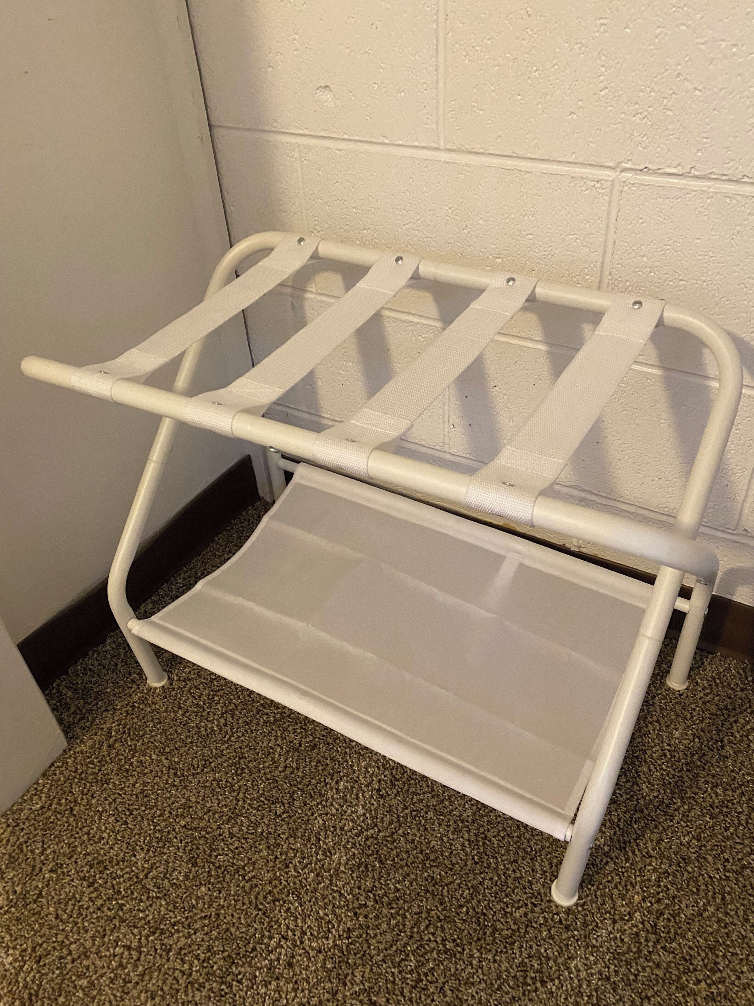 A white metal shelf unit with a flat surface and a slanted shelf against a wall.