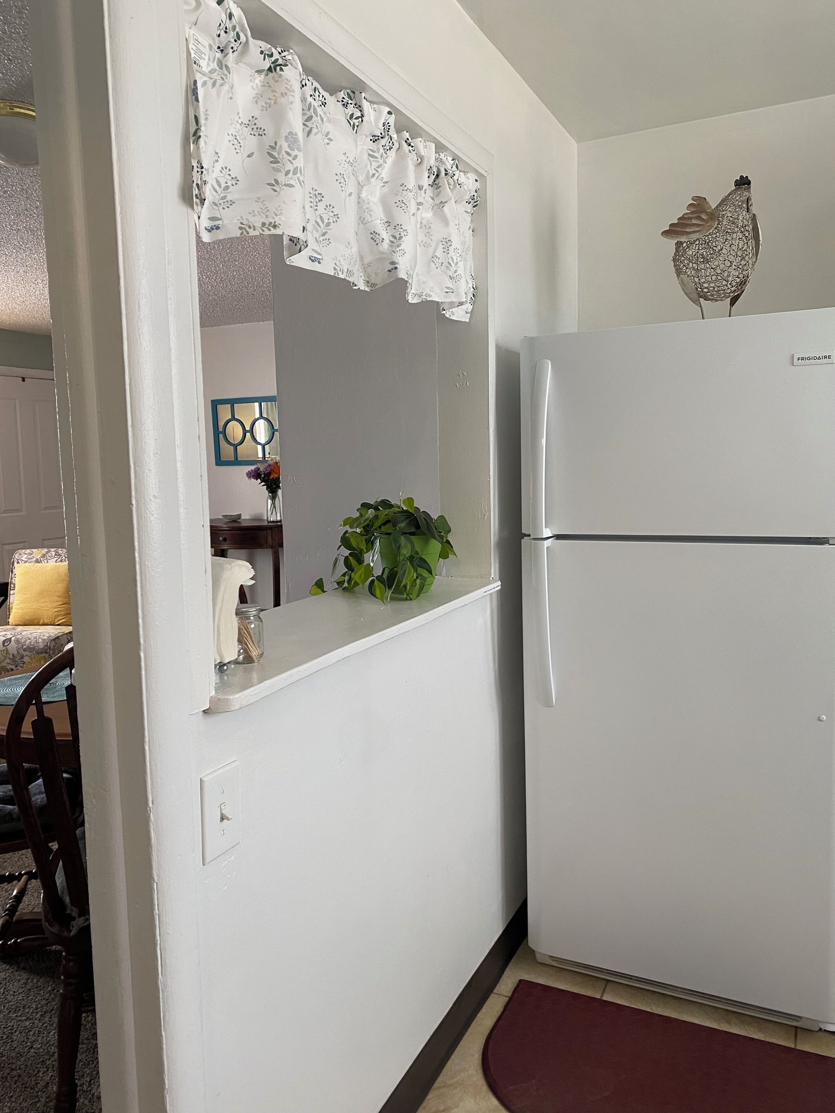 A kitchen with a white refrigerator, a potted plant on the counter, and a decorative item on top of the fridge.