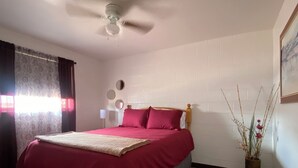 Ein Schlafzimmer mit einem Bett, einem Deckenventilator, einem Nachttisch, einem wandmontierten Spiegel und einer Pflanzvase.