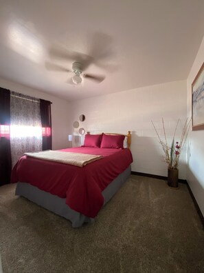 A bedroom with a bed, a ceiling fan, a bedside table, a wall-mounted mirror, and a vase with plants. - Cozy 3-bdrm, 1 bath apt. minutes away from Horseshoe Bend and Antelope Canyon! (Page)