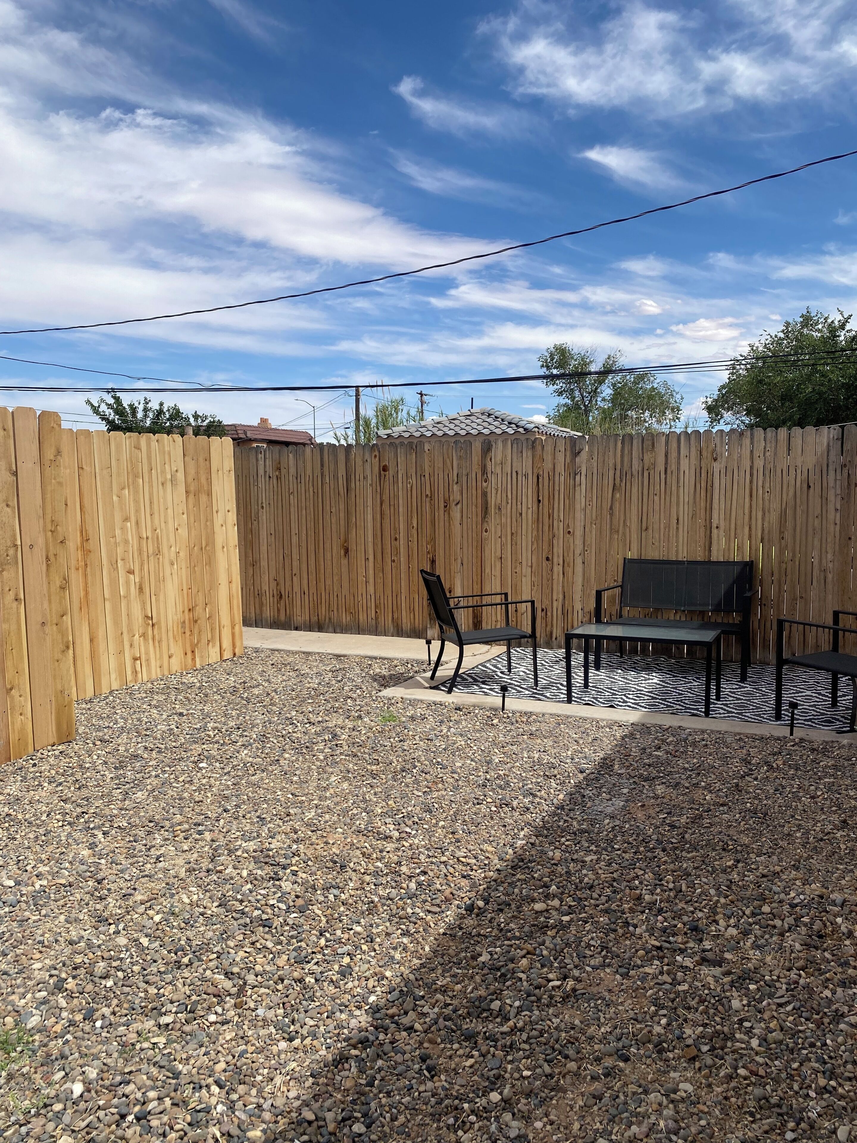 A backyard with a wooden fence, a gravel patio, and outdoor furniture.