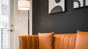 En lædersofa med pude foran en mørk væg, en gulvlampe og en dør med persienner.