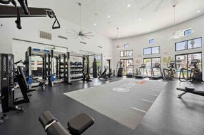 Een ruime fitnessruimte met diverse trainingsapparaten, grote ramen en een plafondventilator.