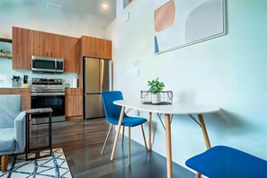 Eine moderne Küche mit Holzschränken, Edelstahlgeräten und einem Essbereich mit weißem Tisch und blauen Stühlen.