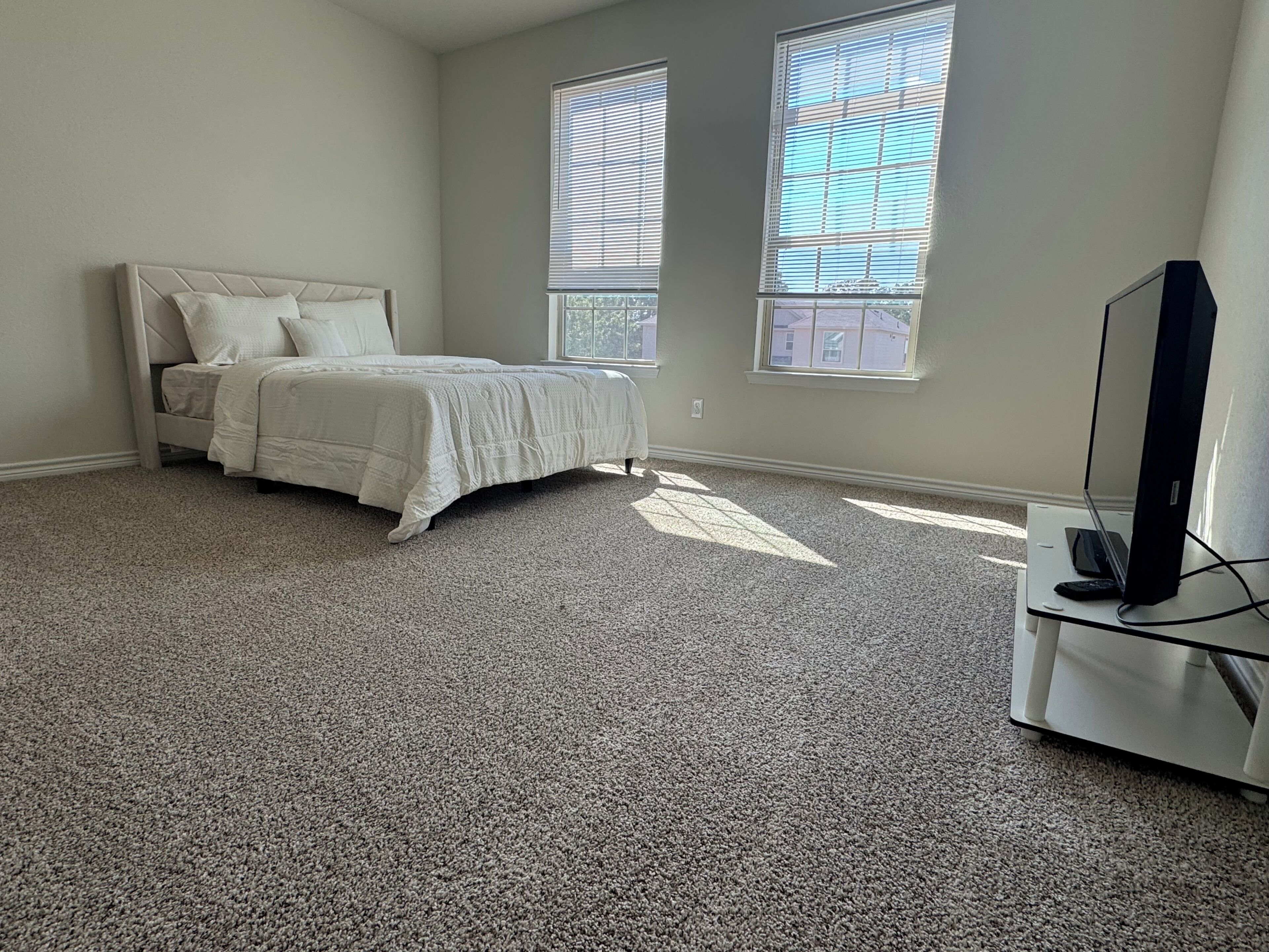 A bedroom with a bed, two windows, and a television on a stand.