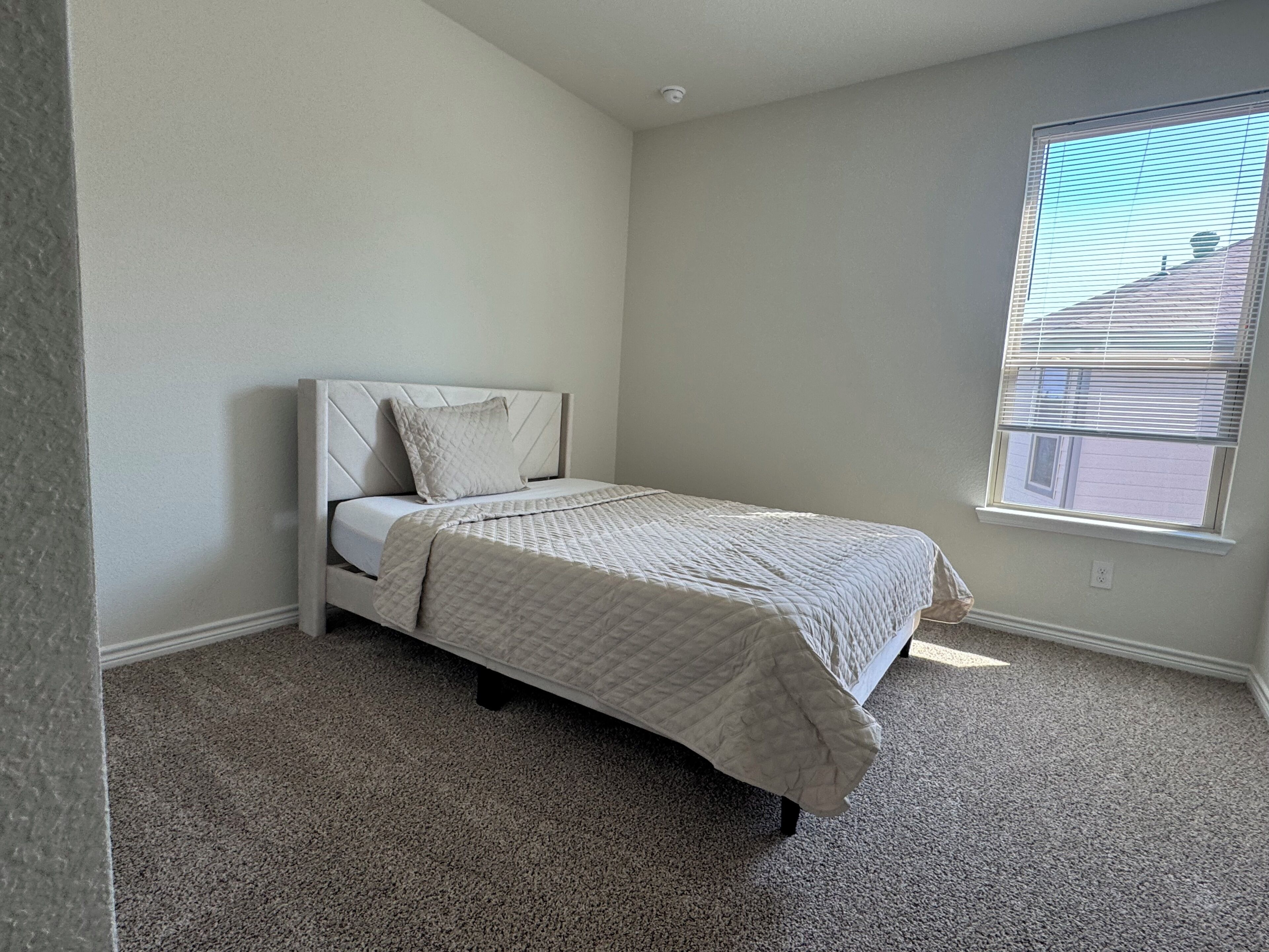 Ein Schlafzimmer mit Bett, Fenster und Teppichboden.