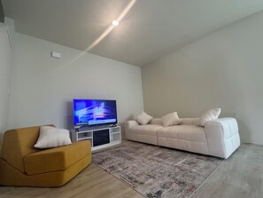 Ett modernt vardagsrum med en platt-TV, en soffa, en fåtölj och en mönstrad matta.