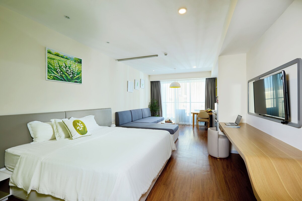 Quarto de hotel com cama, sofá, escrivaninha com laptop, televisão e pintura na parede.