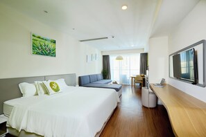 Quarto de hotel com cama, sofá, escrivaninha com laptop, televisão e pintura na parede.
