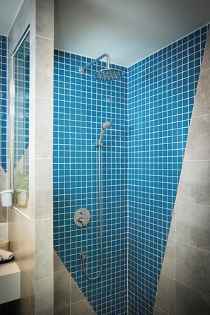 Área de chuveiro com paredes em azulejos azuis, chuveiro manual e torneira fixada na parede.