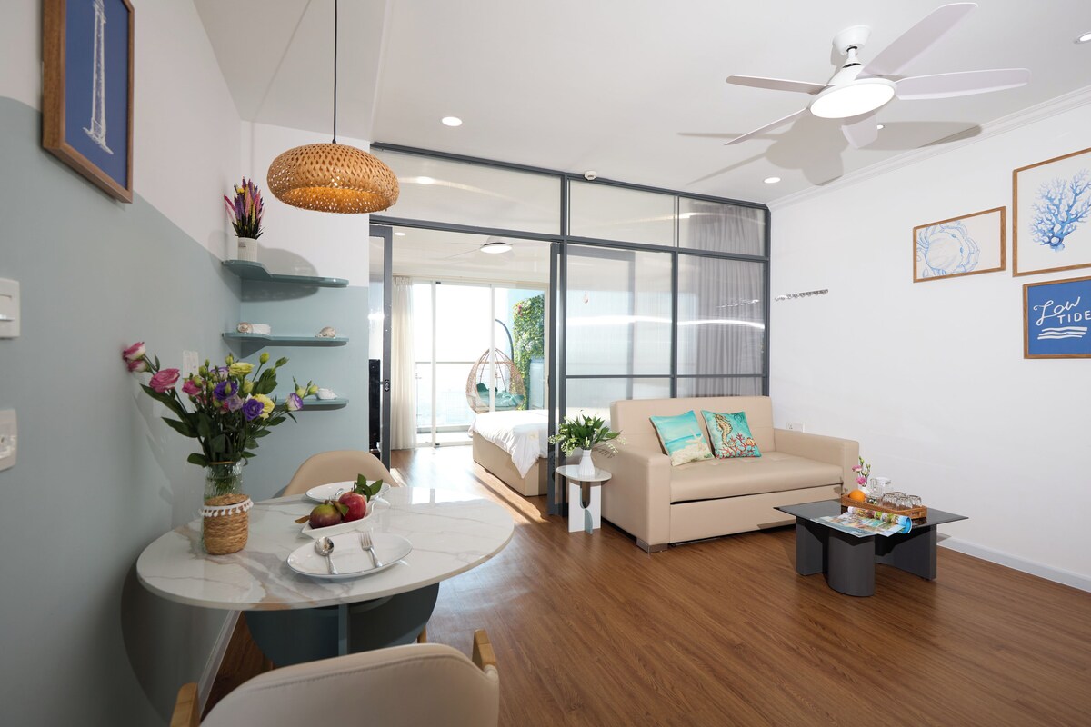 Uma sala de estar moderna com um sofá, uma mesa de jantar com um vaso de flores e um ventilador de teto.