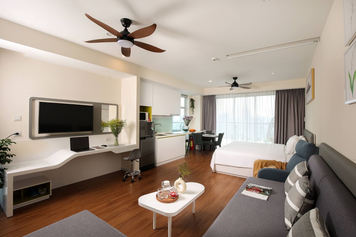 Quarto de hotel moderno com televisão de ecrã plano, secretária com um computador portátil, zona de refeições e uma cama.