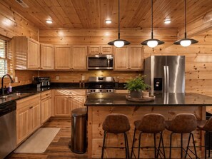 A modern kitchen with wooden cabinets, stainless steel appliances, and pendant lighting. - Indoor Pool • Hot Tub • Theater • Games • Views (Sevierville)