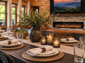 A dining table set with plates, glasses, and candles, with a vase of greenery and a bowl of fruit in the background. - Indoor Pool • Hot Tub • Theater • Games • Views (Sevierville)