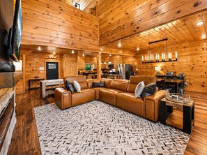 Interior de cabana de madeira com sofá seccional, tapete com padrão herringbone e área de jantar com mesa e cadeiras.