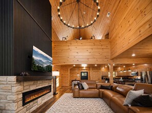 A spacious living area with a stone fireplace, leather sofa, and a large wooden ceiling. - Indoor Pool • Hot Tub • Theater • Games • Views (Sevierville)