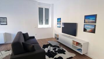 Ein modernes Wohnzimmer mit einem schwarzen Sofa, einem Flachbildfernseher, einer weißen Unterhaltungseinheit und einem Kuhfellteppich.