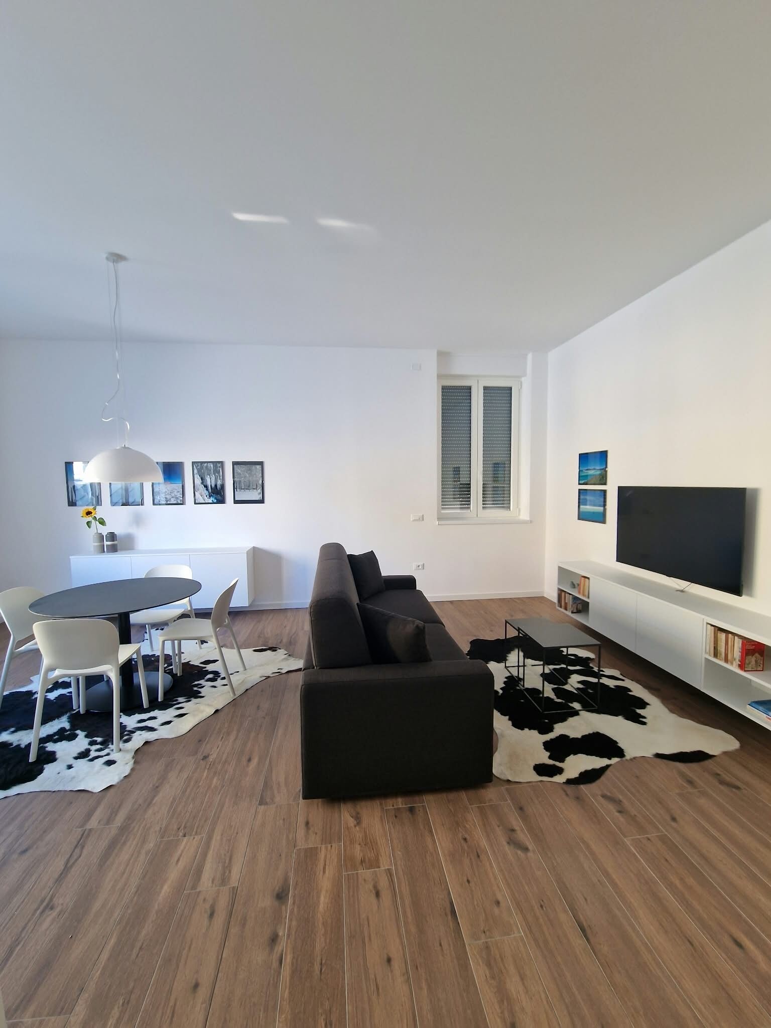 A modern living room with a sofa, dining table, chairs, a TV, and artwork on the walls.