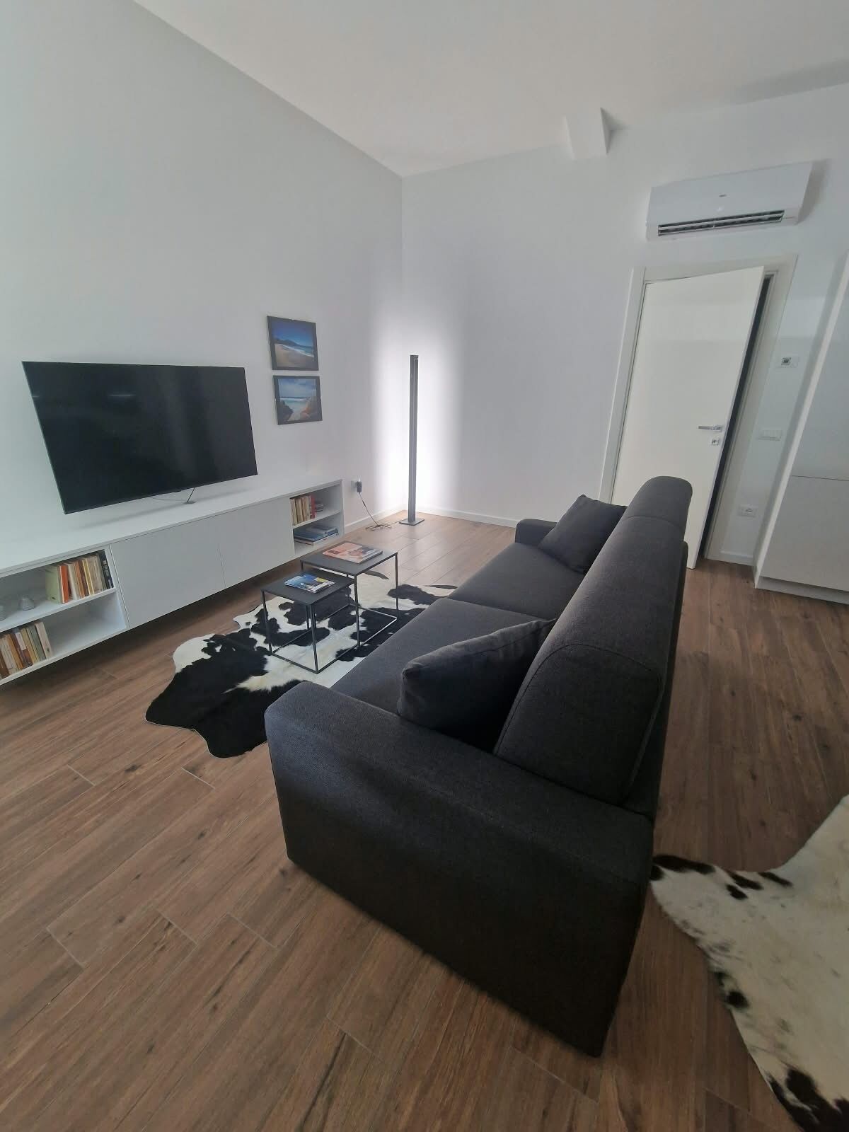 Ett modernt vardagsrum med en stor TV med platt skärm, en grå soffa, ett soffbord och en svartvit matta.