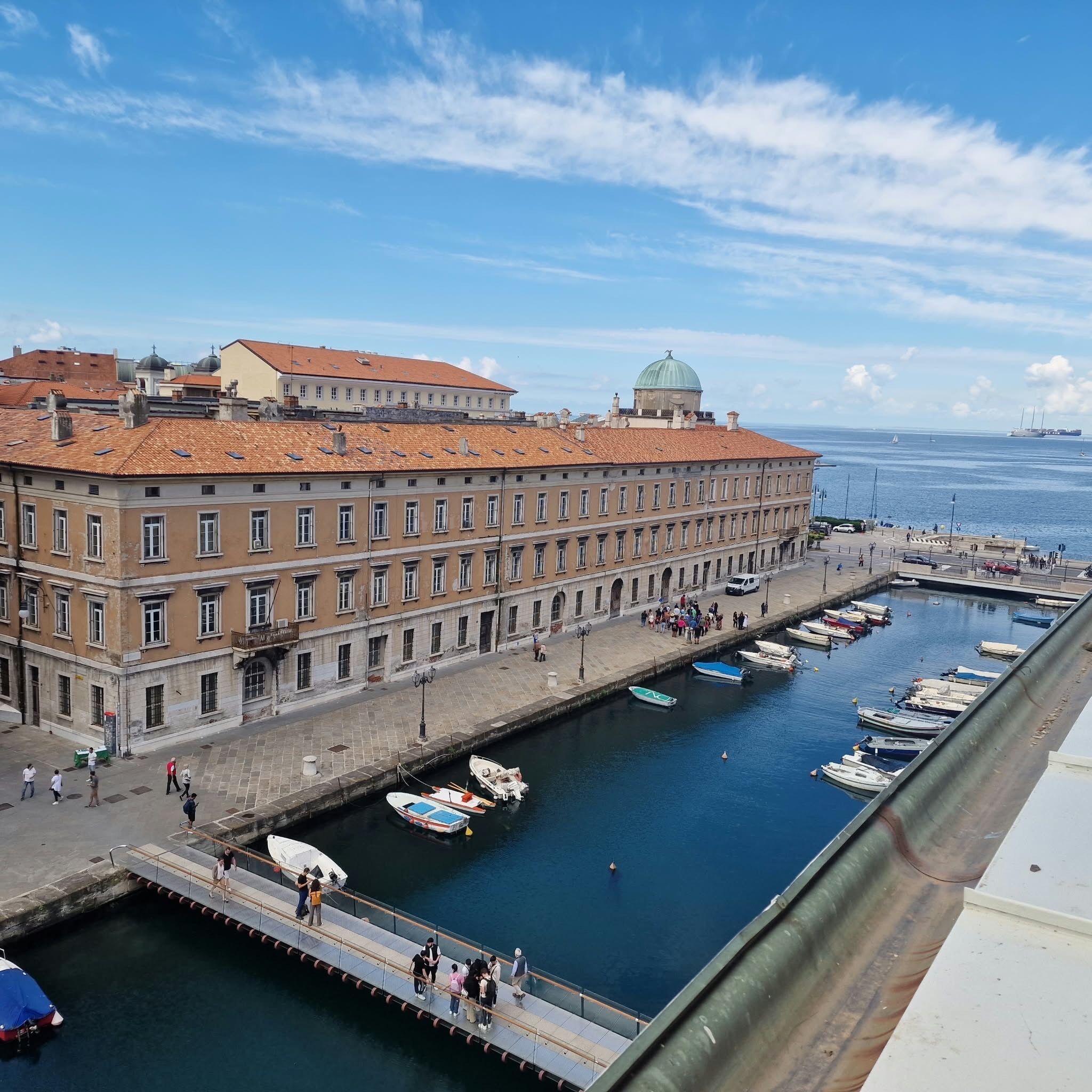 Ein Gebäude am Wasser mit einer langen Fassade, ein Hafen mit Booten und ein klarer Himmel.