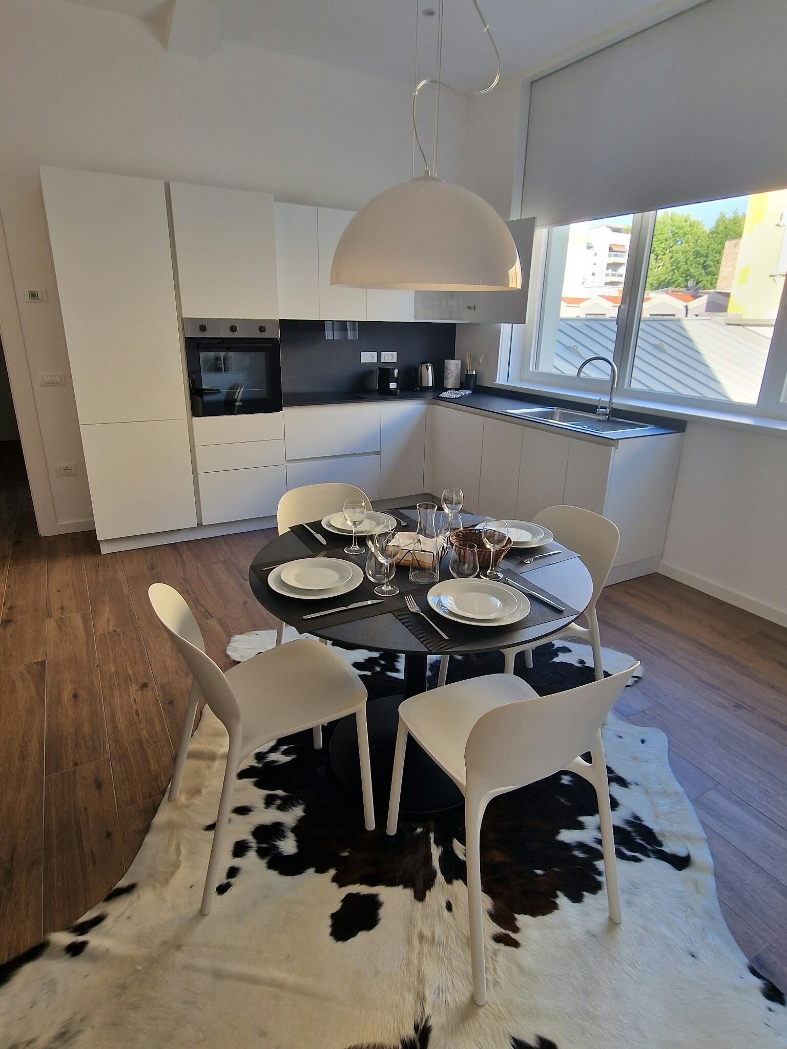Une cuisine moderne avec des meubles blancs, un four encastré et un coin repas agrémenté d’une table ronde prévue pour quatre personnes.