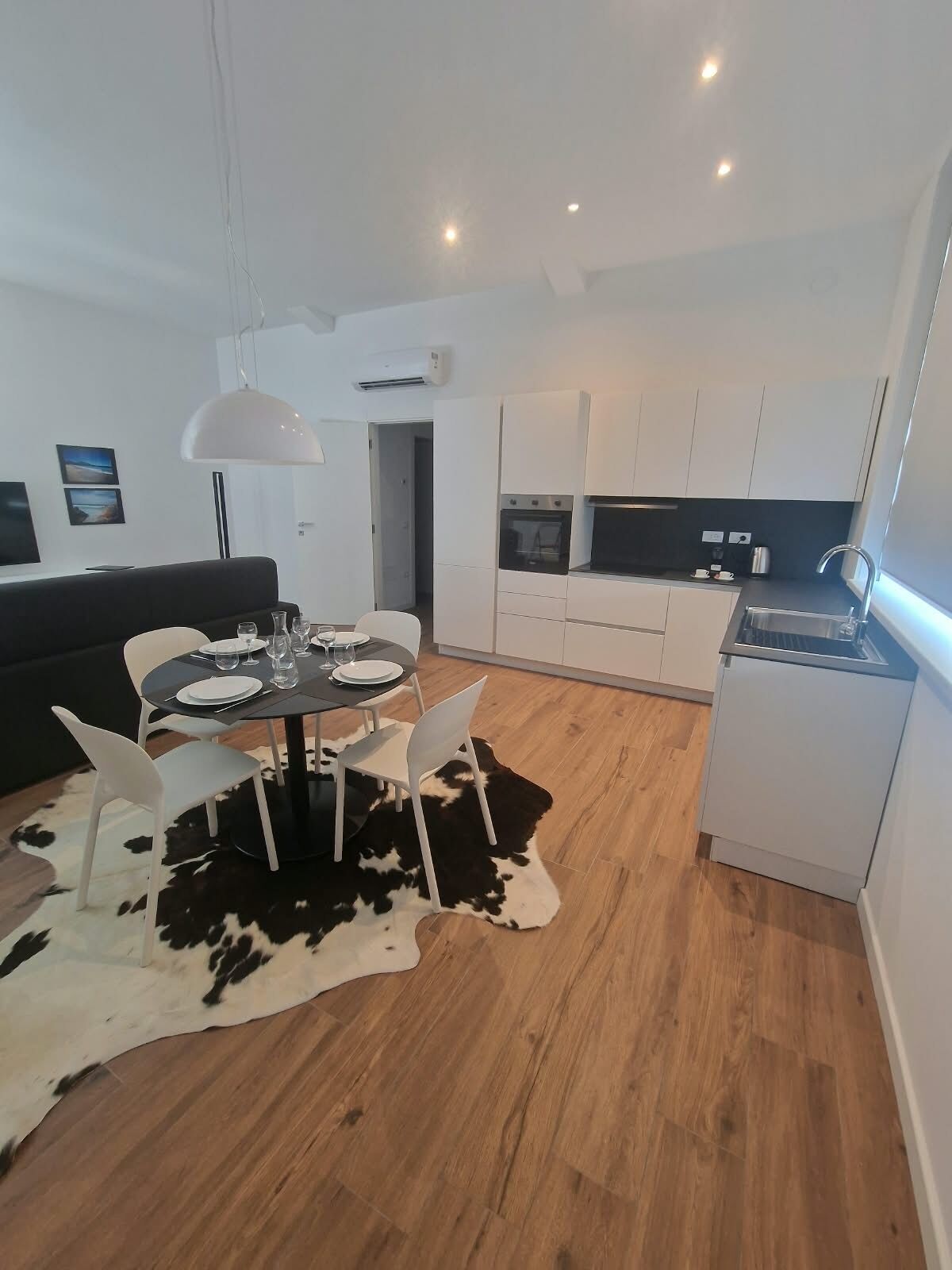 A modern kitchen with white cabinets, a dining area with a round table and chairs, and a black and white cowhide rug.