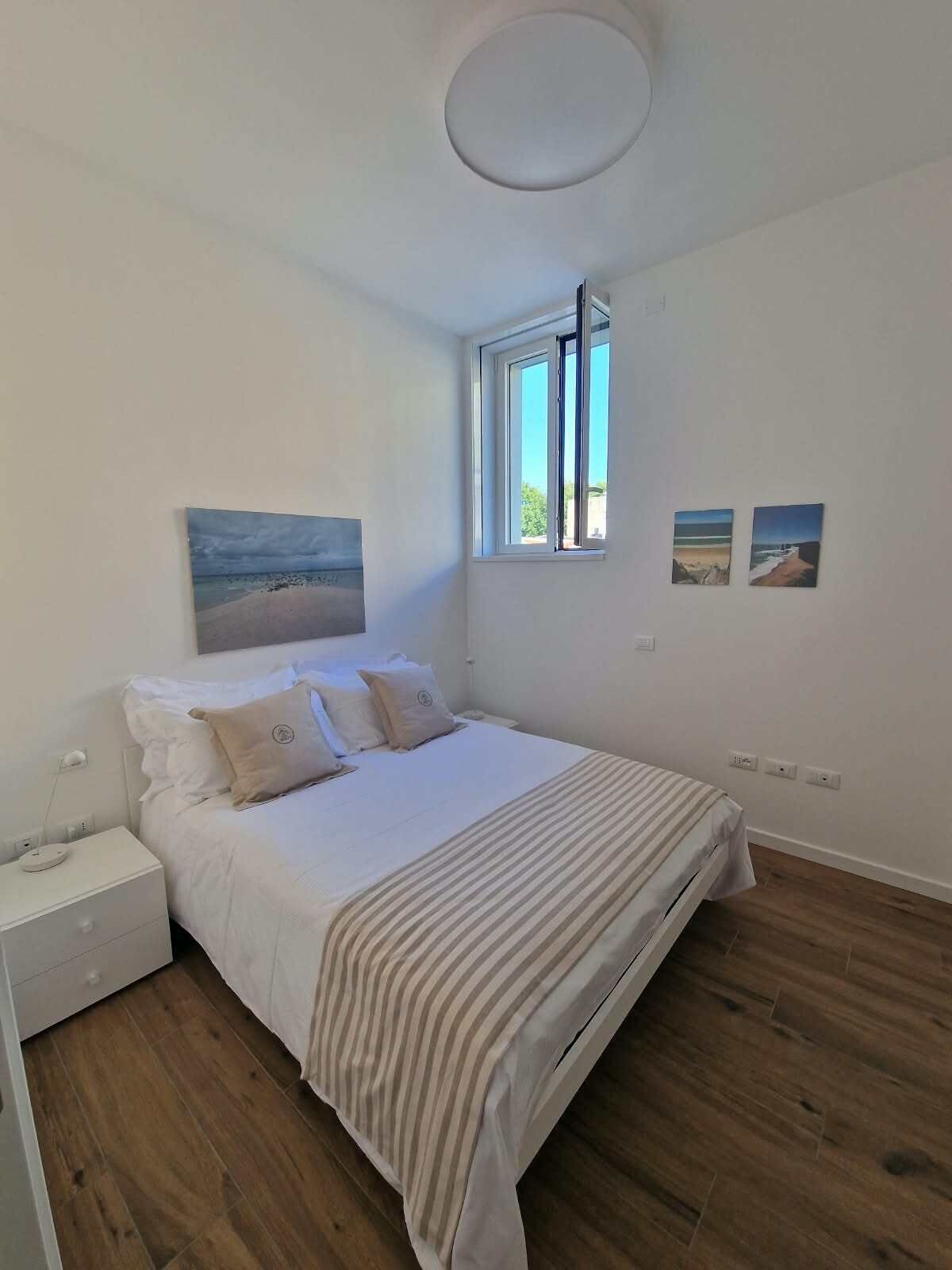 Ein Schlafzimmer mit einem Bett, einem Nachttisch, einem Fenster und zwei Bildern an der Wand.