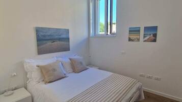 Ein Schlafzimmer mit einem Bett, einem Nachttisch, einem Fenster und zwei Bildern an der Wand.