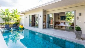 A modern poolside area with a clear pool, lounge chairs, and a glass-enclosed room with a bed. - Kaizer Pool Villas (Thalang)