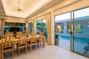 A modern interior with a dining area, a flat-screen TV, and a view of a swimming pool.