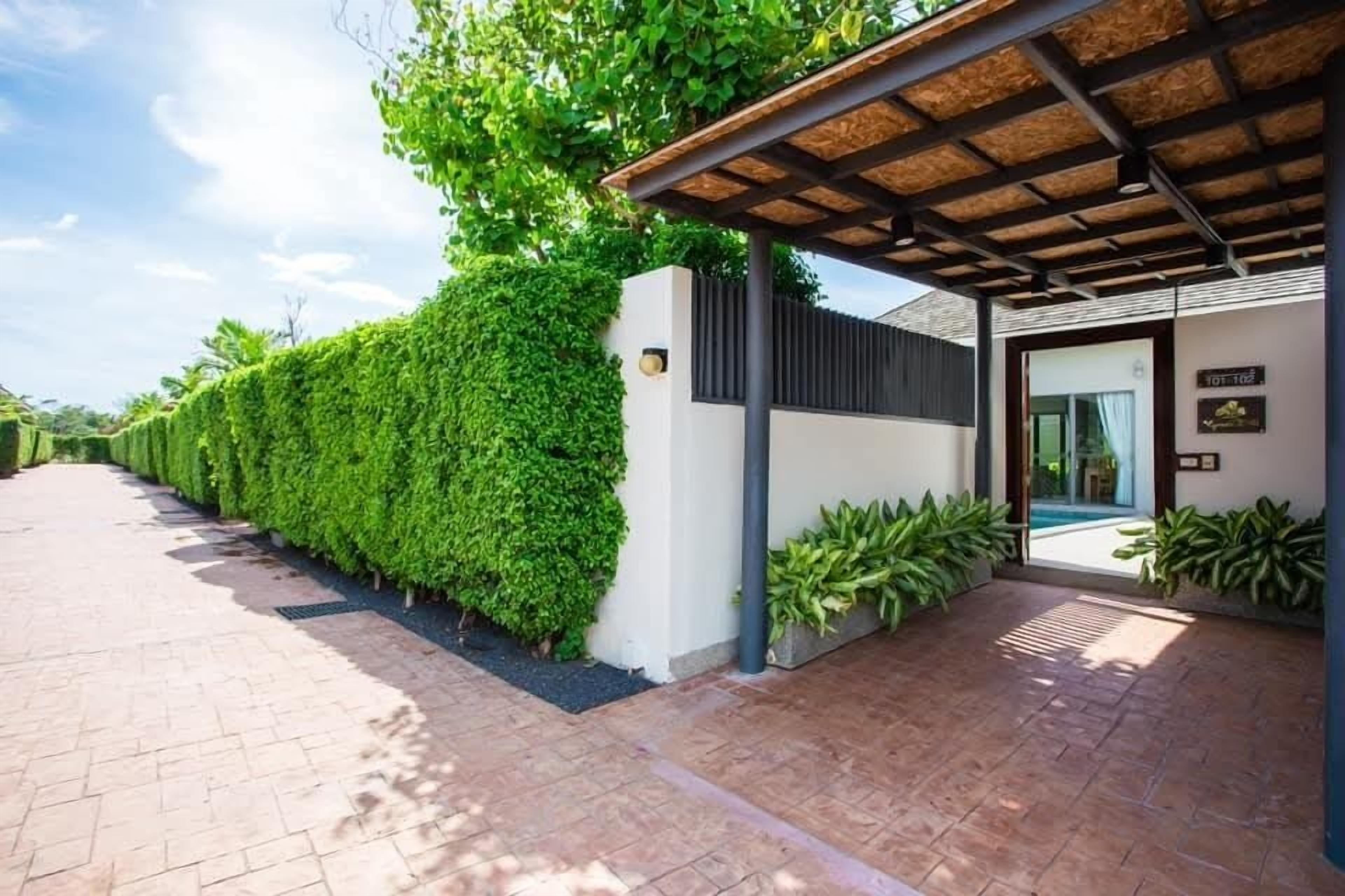 Un edificio moderno con un acceso cubierto, un seto bien cuidado y un camino pavimentado que conduce a la entrada.