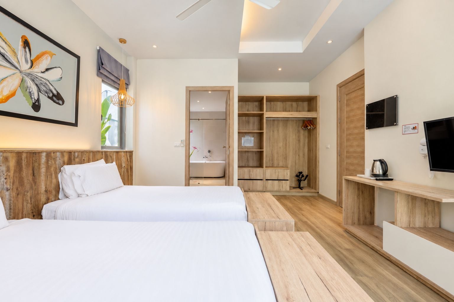 A modern hotel room with two beds, a walk-in closet, a shower area, and a TV mounted on the wall.