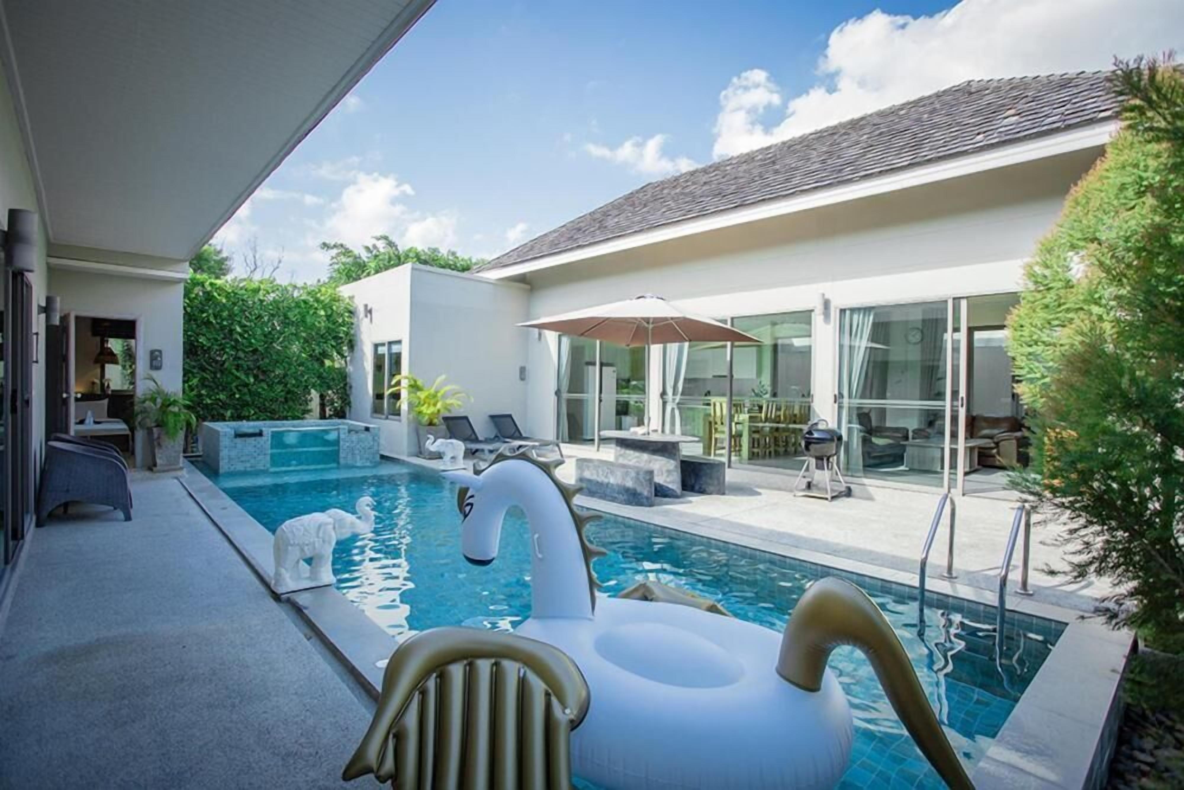 Un espace piscine extérieur moderne, doté d’un gonflable en forme de cygne, de chaises longues et d’un patio fermé par des baies vitrées.