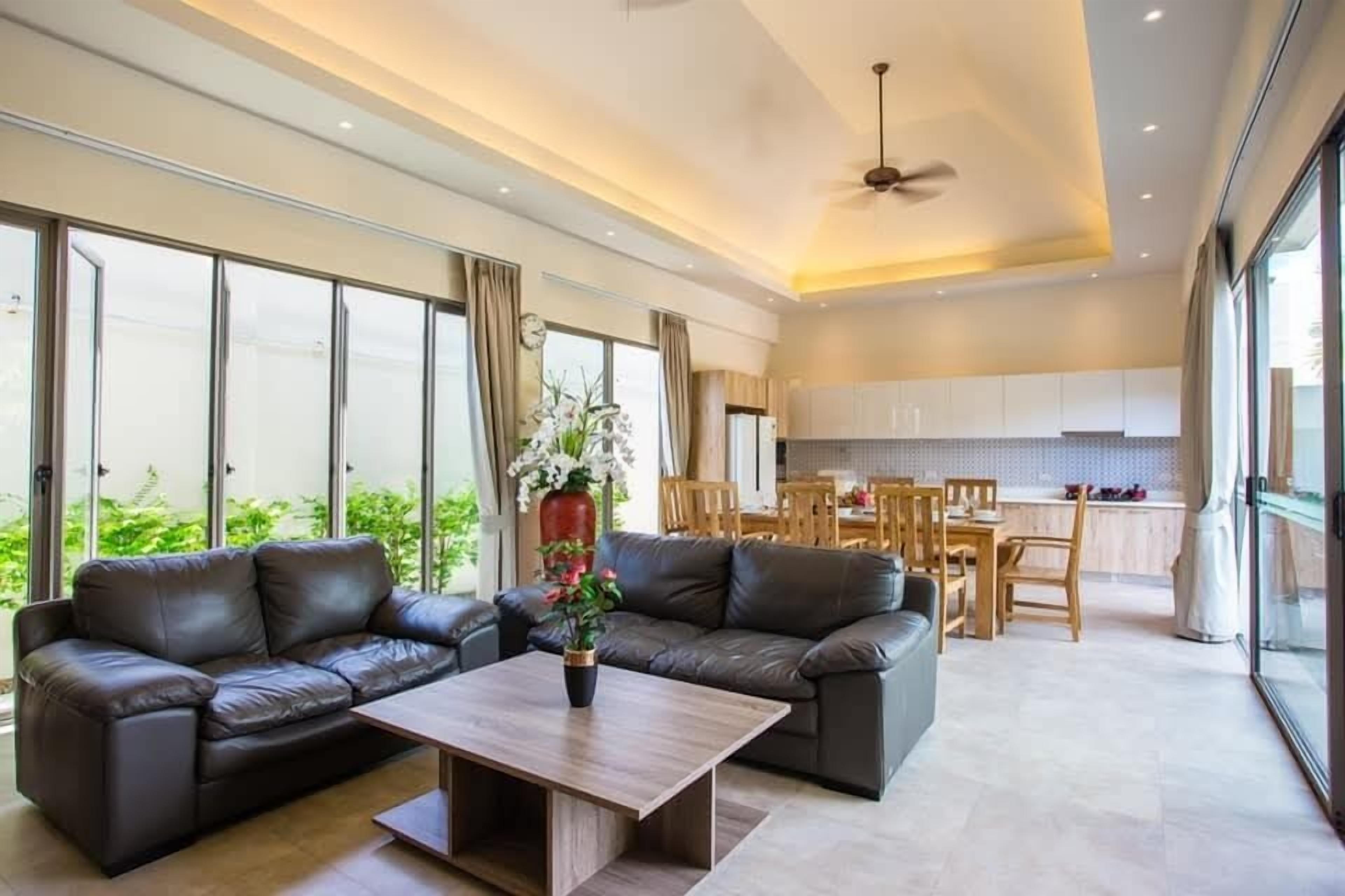 A modern living room with leather sofas, a wooden coffee table, and large windows offering a view of greenery.