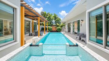 Una piscina con un deck de baldosas, rodeada de sillas de descanso y una pérgola.