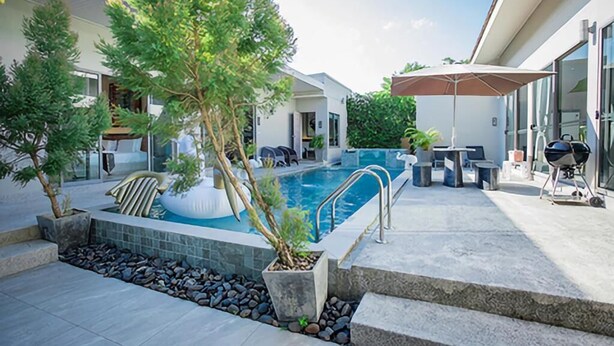 A modern outdoor pool area with a clear sky, surrounded by potted plants, a barbecue setup, and a covered seating area. - Kaizer Pool Villas (Thalang)