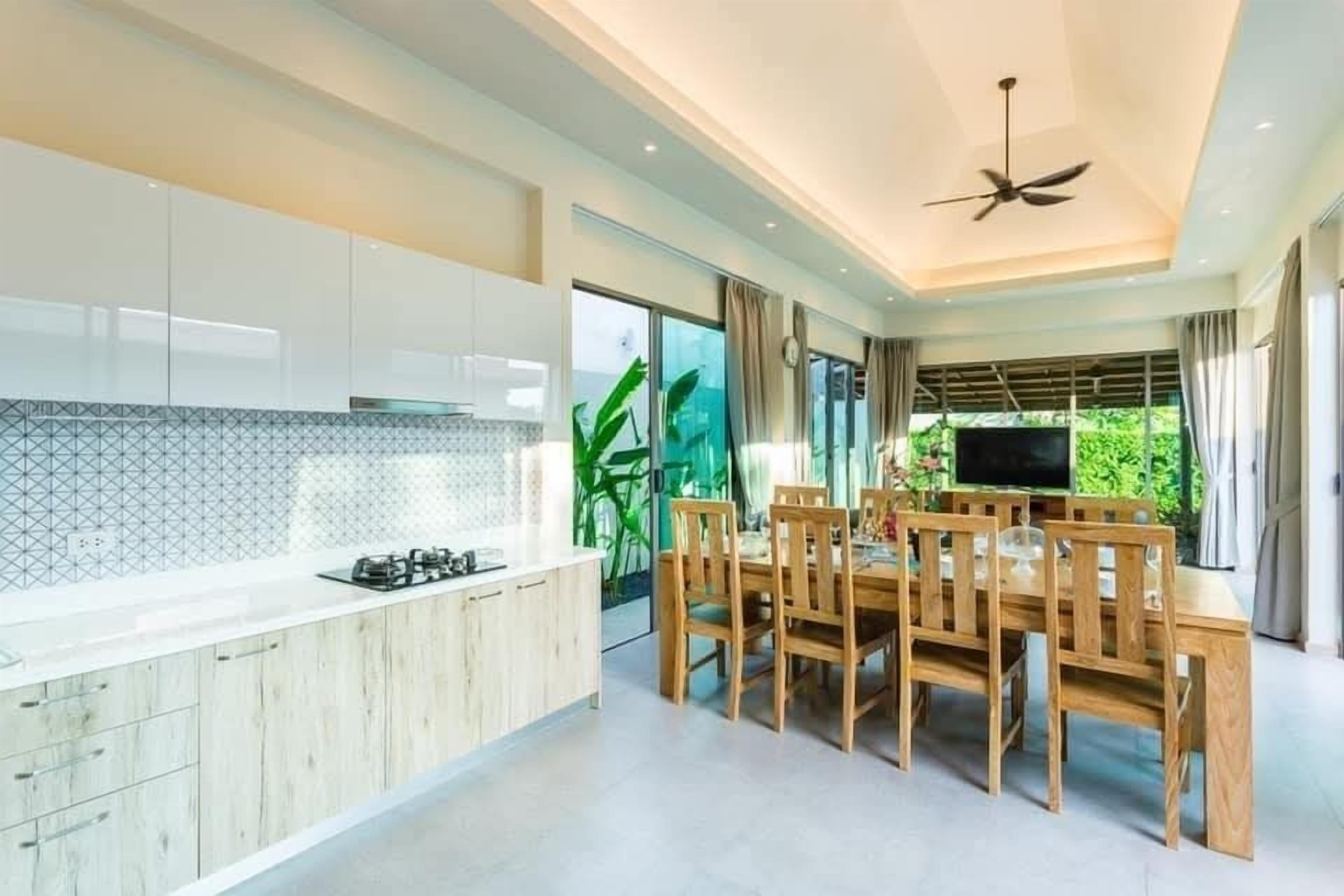 A modern kitchen with a dining area, large windows, and a ceiling fan.