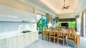 A modern kitchen with a dining area, large windows, and a ceiling fan.