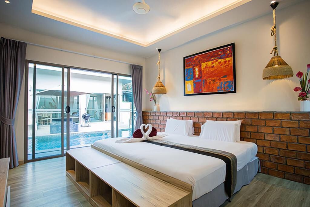 A hotel room with a large bed, a bench, a view of the pool, and a colorful artwork on the wall.