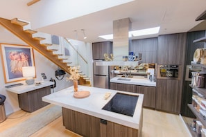 A modern kitchen with a central island, built-in appliances, and a wooden staircase. - Spacious Modern Apartment in the heart of Fitzroy (Melbourne)