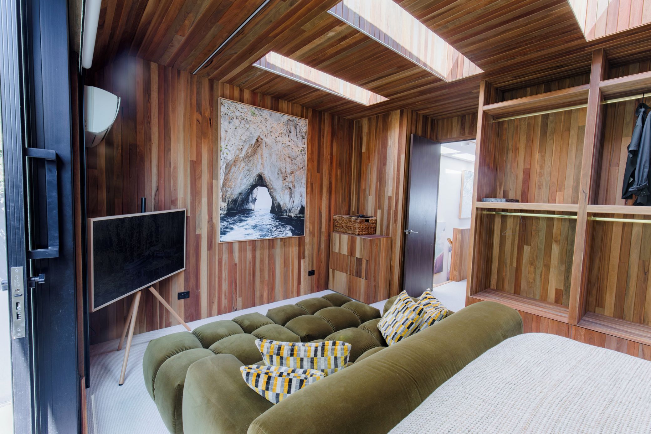A modern room with a wooden interior, a large bed, a sofa, a television, and a painting of a cave.
