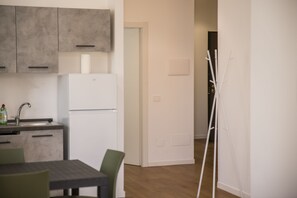 A modern kitchen with grey cabinets, a white refrigerator, and a dining area with a table and chairs. - Hearth City Center Milan (MI)