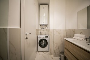 A compact bathroom with a built-in washing machine, a toilet, and a sink with a mirror above. - Hearth City Center Milan (MI)